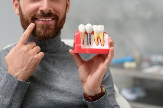 man pointing to his mouth and holding a dental implant mold