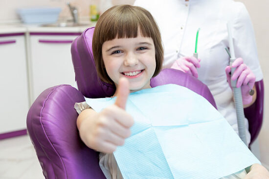 child sitting in a dental chair and giving a thumbs up