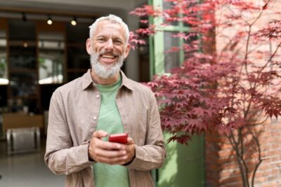 middle-aged man smiling outside while holding his phone