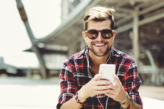 younger man sitting outside on his phone and smiling