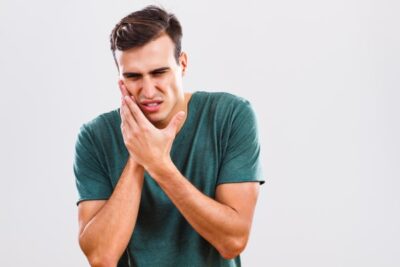 man in green shirt holding his cheek in pain