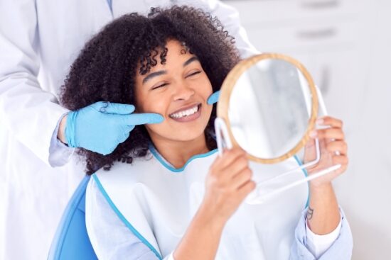 woman smiling and holding a mirror while dentist points to smile