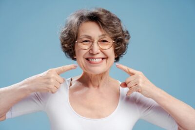 older woman with glasses pointing to her smile