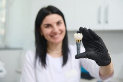 dentist holding a dental implant with her black gloved hand